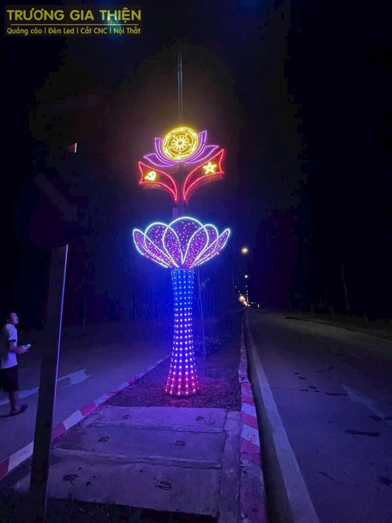 Cột đèn trang trí đường phố, thân và đỉnh gắn đèn LED nhiều màu tạo hình bông hoa phát sáng vào ban đêm.